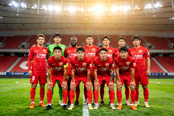 上海海港足球队全家福，球员们身穿红色主场球衣在球场中圈合影